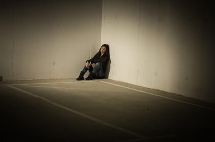 Depressionen, Eine Frau sitzt allein in einer trostlosen halbdunklen Ecke.